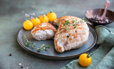 Grilled chicken or turkey breast with cherry tomatoes and thyme on a ceramic plate over green stone background.