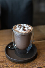 Hot chocolate or cocoa drink with marshmallow in glass cup on wooden table in cafe. Toned image.