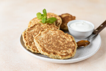 Tasty oatmeal pancakes served with jam and natural yogurt on ceramic plate, light concrete background.