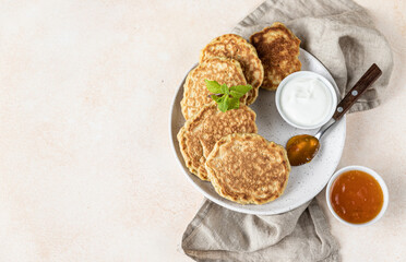 Tasty oatmeal pancakes served with jam and natural yogurt on ceramic plate, light concrete background.
