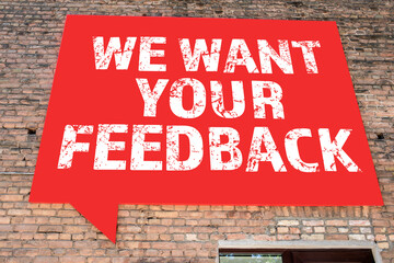 WE WANT YOUR FEEDBACK. Speech bubble advertising banner on a brick wall
