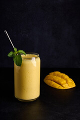 Lassi in glass with tube and mango on dark background vertical orientation. Traditional Indian and Pakistan cold refreshment drink, perfectly quenches thirst 