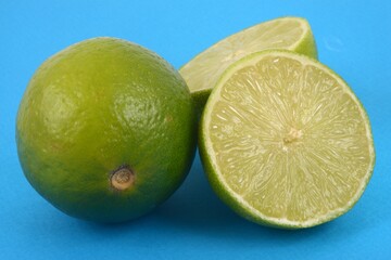 Citrons verts dont un coupé en deux en gros plan sur fond bleu