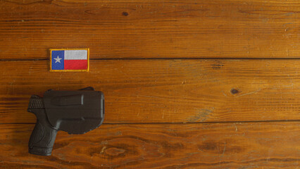 semi-automatic handgun, in holster, below a Texas state flag patch on a textured wooden plank background