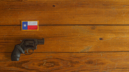 Black snub nosed revolver below a Texas state flag patch on a wooden plank background