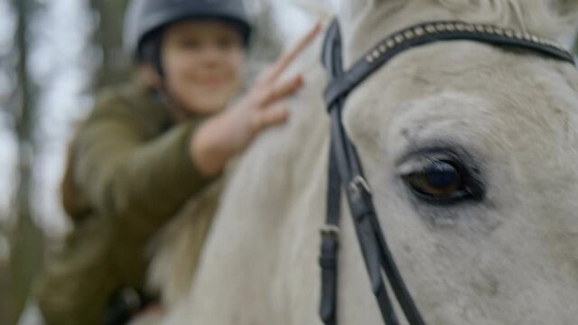 Close up of teen age girl stroking horse in slow motion. Portrait of a girl on horseback, Horse riding camp for children. Child with white horse enjoying ride. Love and friendship concept.