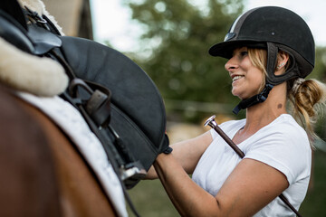 Нappy woman in sports helmet communicates with her horse before training. Sports and health....