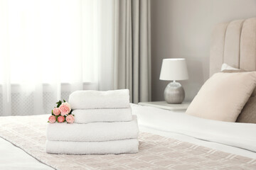 Stack of fresh towels with flowers on bed indoors, space for text