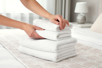 Woman putting fresh towels on bed in room, closeup