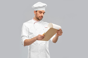 cooking, culinary and people concept - male chef with clipboard and pencil over grey background