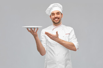 cooking, culinary and people concept - happy smiling male chef in toque holding empty plate over grey background