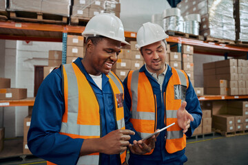 Happy industrial workers in white hardhat and protective vest looking at digital tablet