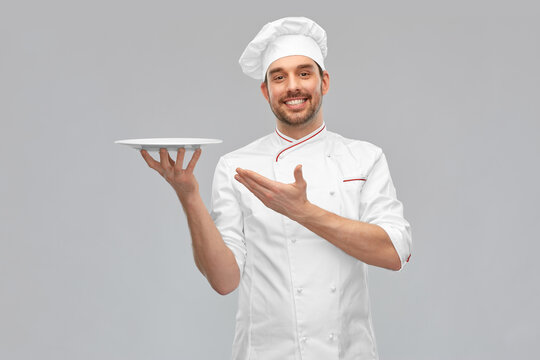 Cooking, Culinary And People Concept - Happy Smiling Male Chef In Toque Holding Empty Plate Over Grey Background