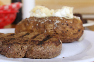 Sirloin Steak With Baked Potato and fresh rolls in background Shallow DOF Focus on Steak