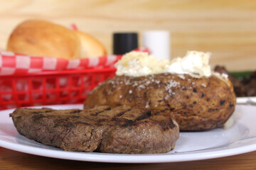 Sirloin Steak With Baked Potato and fresh rolls in background Shallow DOF Focus on Steak
