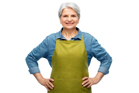 gardening, farming and old people concept - portrait of smiling senior woman in green garden apron over white background