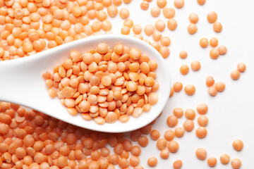 Macro Close-up of Organic masoor dal (Lens culinaris) or whole pink dal on a white ceramic soup spoon. Top view,  over gradient background of itself.