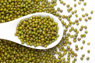 macro Close-up of Organic green Gram (Vigna radiata) or whole green moong dal on a white ceramic soup spoon. Top view, over gradient background of itself.