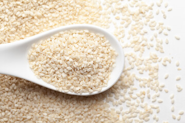 Macro Close up of Organic White  Sesame seeds(Sesamum indicum) polished or white Til without the shell on a white ceramic soup spoon. Top view, over gradient background of itself.