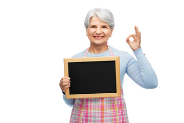 cooking, culinary and old people concept - portrait of smiling senior woman in kitchen apron holding chalkboard and showing ok gesture over white background