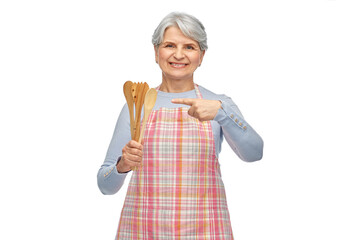 food cooking, culinary and old people concept - portrait of smiling senior woman in kitchen apron with wooden spoons over white background