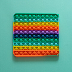 Bright silicone striped toy big Pop It closeup on blue background. Popit for kids playing with rainbow, pressing the bubbles with his fingers, top view. New antistress toy for children and adult