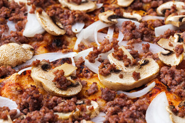 Close-up of pizza topped with mushrooms, onion and chopped meat. Macro shot of delicious products. Selective focus.