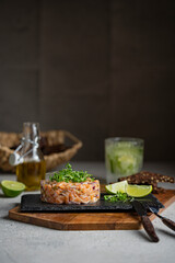 Fototapeta na wymiar Salmon fish tartare with micro greens, lime on black stone plate, dark background. Grey textured table, healthy sea food concept. Macro shot with copy space.