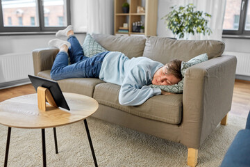 people, boredom and depression concept - bored or lazy young man with tablet pc computer lying on...