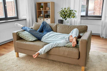 people, boredom and depression concept - bored or lazy young man lying on sofa at home