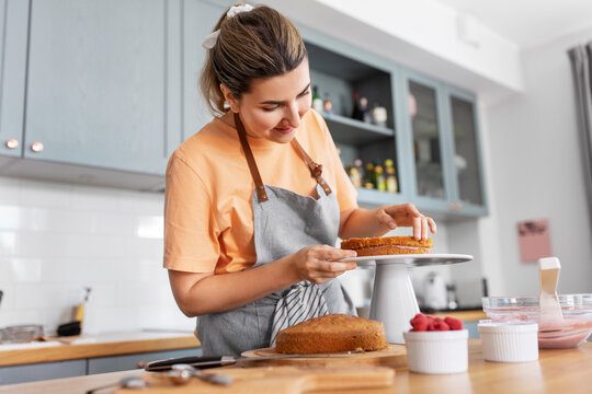 Culinary, Baking And Cooking Food Concept - Happy Smiling Young Woman Making Layer Cake On Kitchen At Home