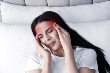 Young woman suffering from migraine in bed, above view