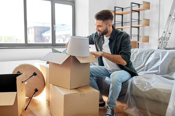 moving, people and real estate concept - happy smiling man unpacking boxes at new home