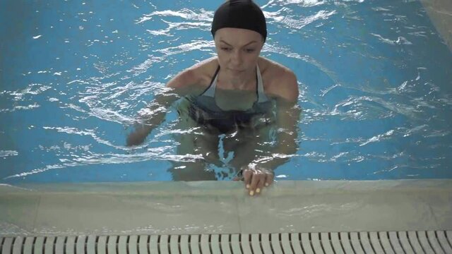 High angle view of armless woman in cap swimming in pool
