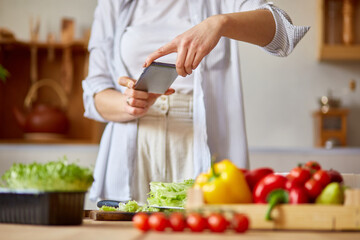Woman taking photo of healthy salad with smartphone for her blog on kitchen at home, Food blogger concept, healthy lifestyle.