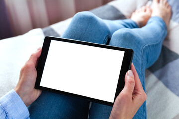 Woman holding digital tablet with blank white desktop screen sitting on the bed. Tablet blank screen mockup. Close-up. Copy space.