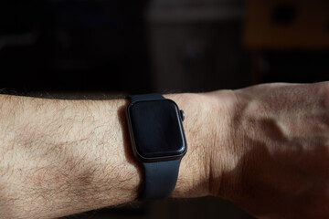 Black smart watch on a man's hand, black screen, dark background.