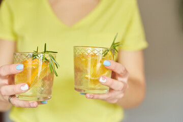 Female woman hand hold two glasses of citrus orange and rosemary fresh lemonade