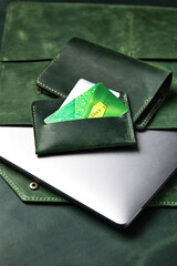 Leather case for a laptop, wallet, business card holder from green leather, handmade products on a wooden table, top view, close-up.
