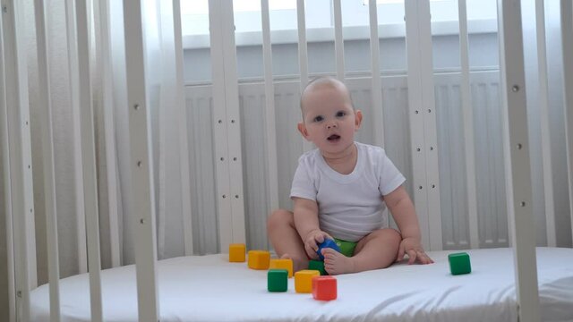 A small child plays in his crib with colored cubes and builds a pyramid out of them.
