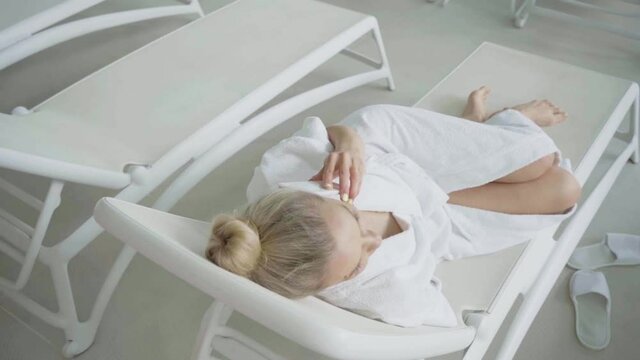 Woman with amputated arm talking on smartphone on deck chair in spa center