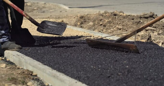 The pouring asphalt worker uses a shovel to level and smooth the hot asphalt on the floor in the road construction site. Seal coating is a street maintenance technique that preserves the condition of