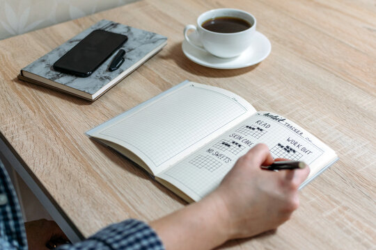 Bullet Journal, Habit Tracker. Female hand notes in habits tracker. Woman cross off day with routine in her Habit Tracker. Selective focus