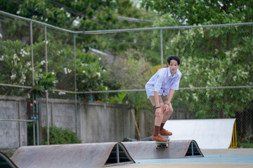 Teen Asian Skater boy in student uniform skating in the local skate park.