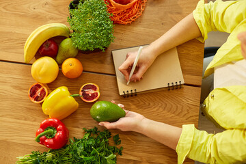 Woman planning, writing weekly meals on a meal planner note or diet plan