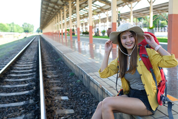Asian traveller with red backpack and her hat sitting on train railway.