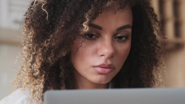 A close-up view of a serious african american woman is using her laptop computer while working at home