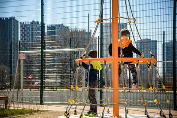 Fototapeta premium Two young boy active little child playing climbing at spring metal playground his hand to exercise at outdoor. Warm sunny day. Friendship concept