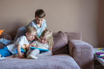 children play with tablet while sitting on the couch at home. child plays games with a gadget. games on the tablet for children. children's leisure at home