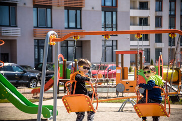 Two European boys swing on a swing in the summer holidays. Children have fun outdoors